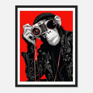 May include: A framed art print featuring a chimpanzee wearing a black leather jacket, sunglasses, and a beanie, holding a vintage camera. The background is a solid red. The image is a stylized illustration.