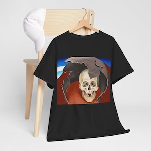 May include: Black t-shirt with a skull graphic. The design shows a skull breaking through a cracked, dark grey sphere against a red and blue backdrop. The t-shirt is displayed on a wooden hanger.