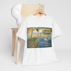 Könnte beinhalten: Weißes T-Shirt mit einem surrealistischen Gemälde, das schmelzende Uhren, ein Gitter und eine Küstenlandschaft zeigt. Das Kunstwerk verwendet Blau-, Gelb- und Brauntöne. Eine weiße Baseballkappe hängt an einem Holzstuhl.