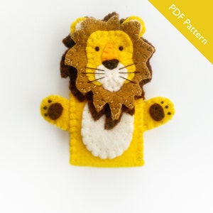 May include: A handmade felt lion puppet with a yellow body, brown mane, and white accents. The puppet has a smiling face with black whiskers and the text "PDF Pattern" in a yellow banner.