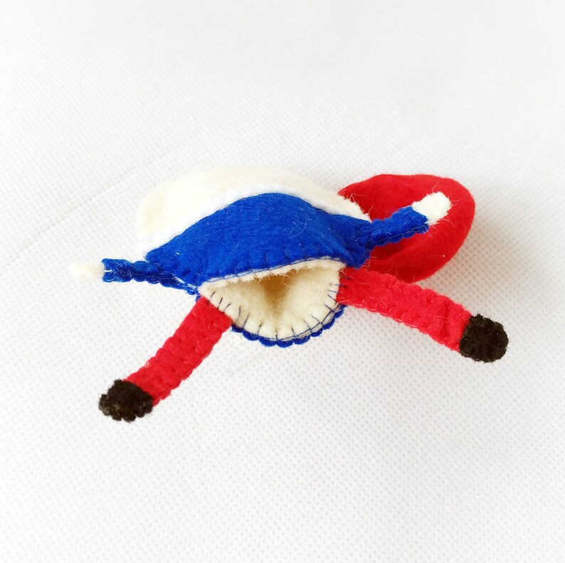 Puede incluir: Una mu&ntilde;eca de fieltro hecha a mano con un dise&ntilde;o caprichoso. La mu&ntilde;eca presenta un sombrero y piernas rojas, una cubierta para la cabeza blanca y azul y pies negros. La mu&ntilde;eca est&aacute; hecha de fieltro y tiene un dise&ntilde;o cosido.