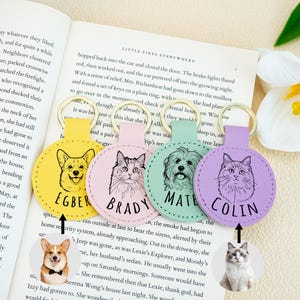 May include: Four colorful keychains with pet portraits: a yellow Corgi keychain with "EGBER", a pink cat keychain with "BRADY", a green dog keychain with "MATE", and a purple cat keychain with "COLIN". Each keychain has a gold ring.