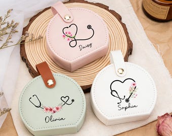 May include: Three round, pastel-colored cases with a stethoscope design and floral accents. Each case has a different name: Daisy, Olivia, and Sophia. The cases have a handle and are on a wooden slice.