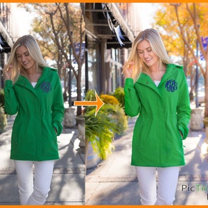 May include: A green hooded jacket with a white monogram on the front. The jacket is worn by a person standing on a sidewalk in front of a building.