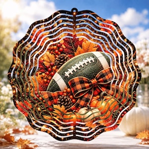 May include: A circular metal wind spinner featuring a fall-themed design with a football, orange and white pumpkins, pinecones, red berries, and autumn leaves. A black and orange plaid ribbon is tied around the football in the center.