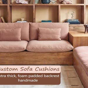 May include: A custom sofa with thick, foam-padded cushions in a muted rose colour. The sofa has a wooden base and backrest, with two matching throw pillows. The image includes text that reads "Custom Sofa Cushions, extra thick, foam padded backrest, handmade."