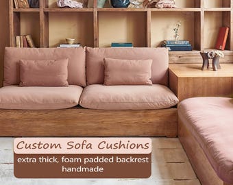 May include: A custom sofa with thick, foam-padded cushions in a muted rose colour. The sofa has a wooden base and backrest, with two matching throw pillows. The image includes text that reads "Custom Sofa Cushions, extra thick, foam padded backrest, handmade."