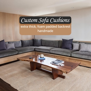 Könnte beinhalten: Ein Ecksofa mit grauen Kissen und Zierkissen. Das Sofa ist in einen Holzrahmen eingebaut. Ein Holztisch steht vor dem Sofa auf einem beigen Teppich. Der Text lautet "Custom Sofa Cushions extra thick, foam padded backrest handmade."