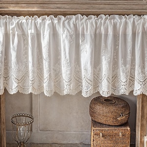 Puede incluir: Valance de encaje blanco con borde festoneado, colgando sobre un marco de ventana de madera. La cenefa está decorada con delicados bordados.