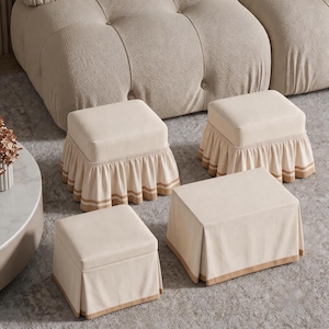 May include: Four beige ottomans with varied base designs. Two feature gathered fabric skirts with horizontal tan stripes, while the other two have smooth, pleated fabric covers with solid tan trim along the bottom edges, all in a neutral tone.