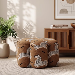 May include: A brown, textured, four-lobed ottoman featuring a repeating pattern of white and black zebras. The piece has a soft, fleece-like surface and a rounded, segmented shape, providing a low-profile seating or footrest option.