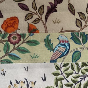 May include: A close-up of three fabric swatches with floral and bird patterns. The top swatch features a beige background with orange and purple flowers and a brown bird. The middle swatch features a light green background with green leaves, a brown branch, and a blue and pink bird. The bottom swatch features a white background with green leaves and a white flower.