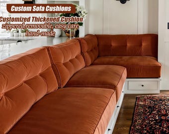 May include: A bespoke, terracotta-coloured sofa with thick, buttoned cushions. The sofa is L-shaped, with a curved section. The cushions are zipped and removable. The image text reads "Custom Sofa Cushions".