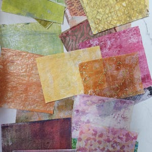 Op de afbeelding: Een verzameling getextureerde, rechthoekige papieren vellen in verschillende kleuren, waaronder groen, oranje, geel en roze. Sommige vellen hebben patronen en texturen, terwijl andere effen zijn. De papieren zijn in een verspreide, overlappende manier gerangschikt.