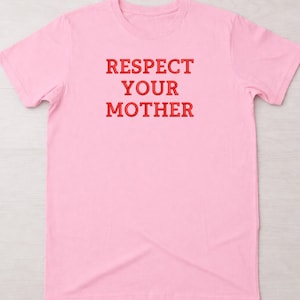 Op de afbeelding: Lichtroze T-shirt met de tekst "RESPECT YOUR MOTHER" in rode, vette letters. Het shirt heeft korte mouwen en een ronde hals.