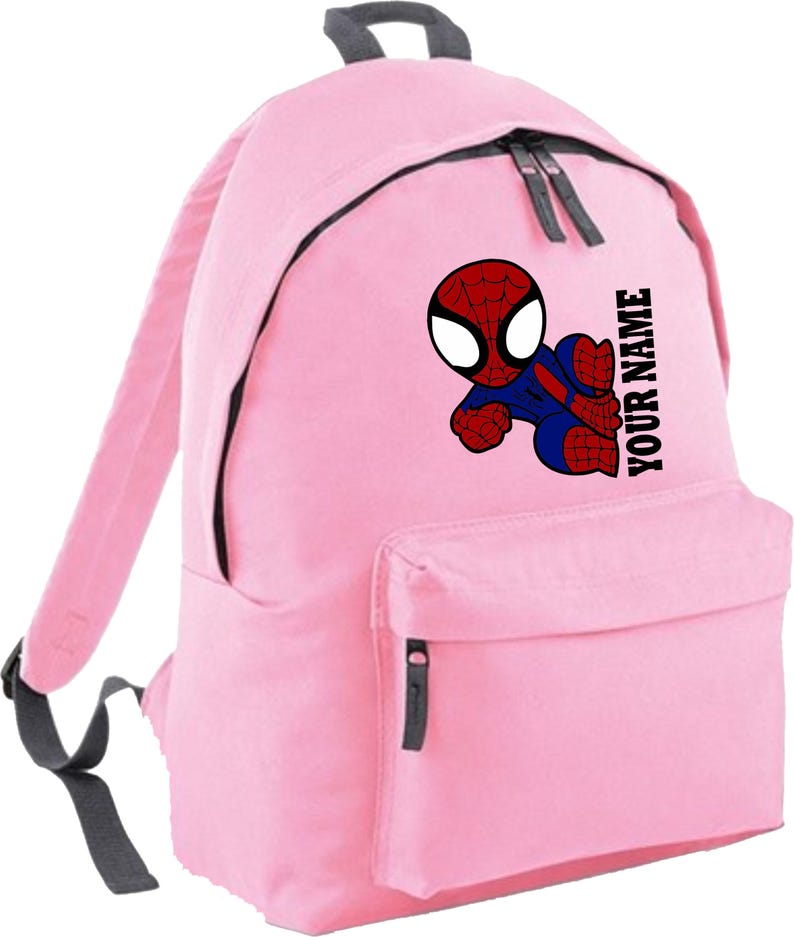 May include: Pink backpack featuring a cartoon Spider-Man graphic in red, blue, and black. The backpack has a front pocket, black zippers, and the text "YOUR NAME" printed vertically. The straps and top handle are gray.