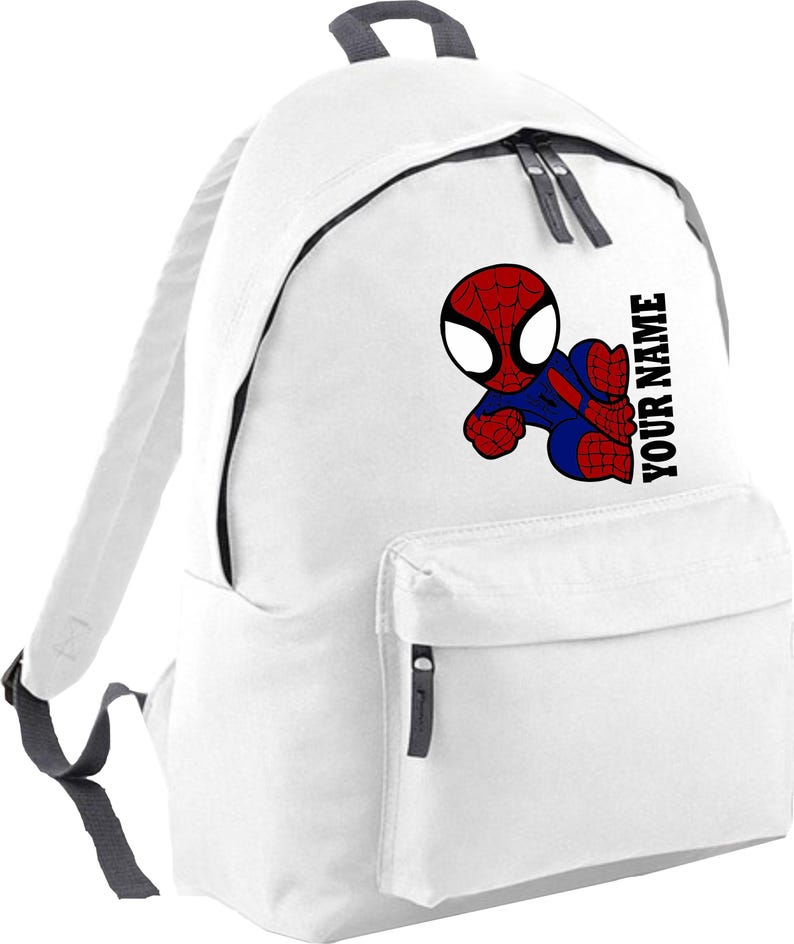 May include: White backpack featuring a cartoon Spider-Man graphic in red, blue, and black. The backpack has a front pocket, a top handle, and the text "YOUR NAME" printed vertically on the side. The straps and zippers are gray.