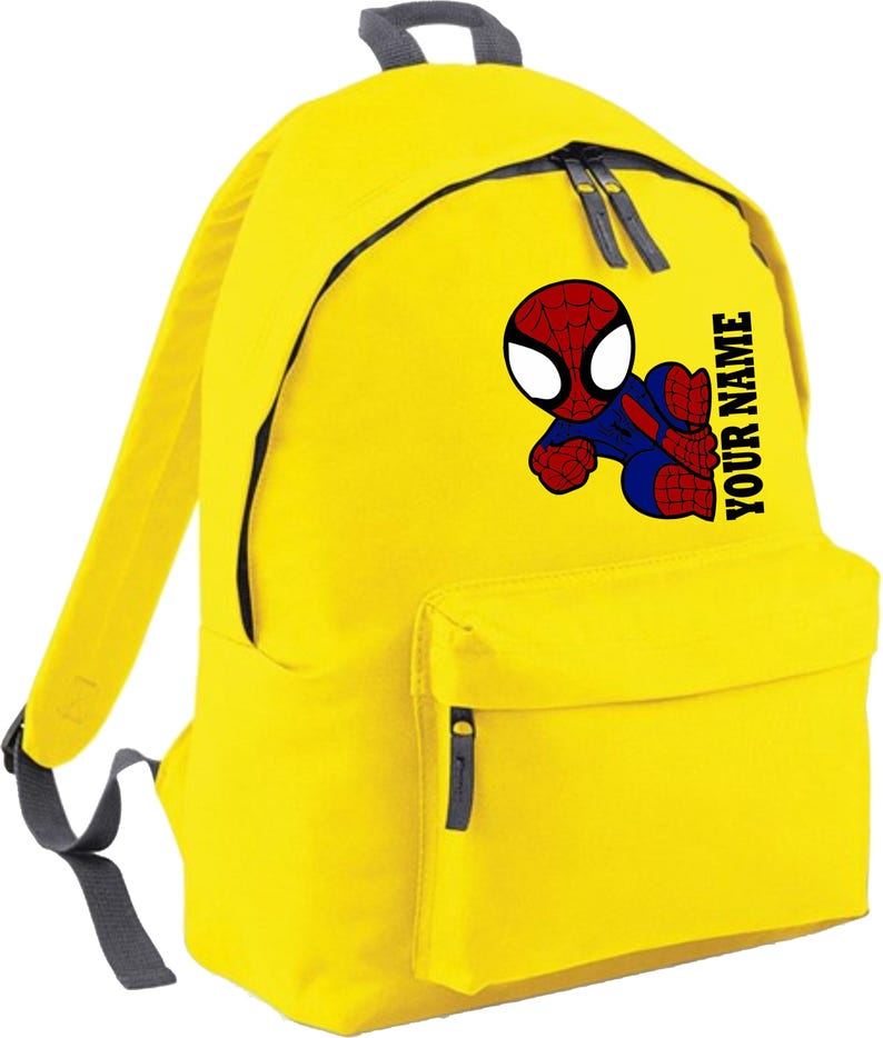 May include: Yellow backpack featuring a cartoon Spider-Man graphic. The backpack has a front pocket, two side straps, and the text "YOUR NAME" printed vertically on the side. The backpack has black zippers and a gray handle.