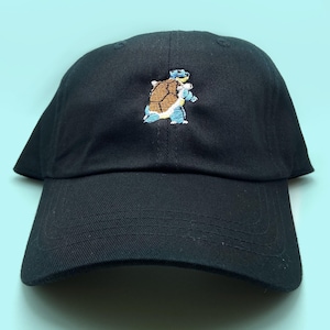 May include: A black baseball cap with an embroidered image of a blue and brown turtle.