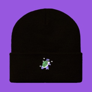 May include: Black beanie featuring an embroidered cartoon turtle in green, purple, and blue. The turtle is surrounded by small white star-shaped accents. The beanie is made of a soft, knitted material.