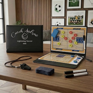 Könnte beinhalten: Ein schwarzes, klappbares Coaching-Board mit der Aufschrift Coach Andrew Lightning Soccer 2026, ausgestattet mit einem magnetischen Basketballfeld-Diagramm, gelben und roten Zahlenmagneten, einem blauen Schwamm, zwei Stiften und einer schwarzen Trillerpfeife.