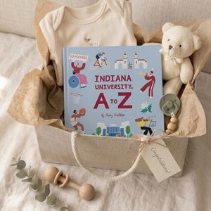 Puede incluir: Una caja de regalo que contiene un body de beb&eacute; color crema, un libro azul claro Indiana University A to Z, un peque&ntilde;o oso de peluche crema, un chupete verde salvia con cuentas de madera y un sonajero de madera, con una etiqueta que dice Congratulations!
