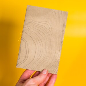 May include: A brown paper notebook with a wood grain pattern. The notebook is held in a hand against a yellow background.