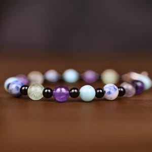 May include: A bracelet made of various colored beads, including blue, green, purple, and black. The beads are strung on a clear elastic cord.