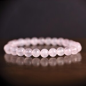 May include: A pink rose quartz beaded bracelet. The bracelet is made of smooth, round beads and is strung on a clear elastic cord.