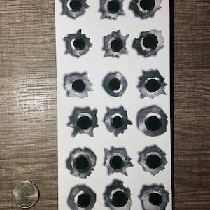 May include: A sheet of 18 white bullet hole stickers. The stickers are black and gray and look realistic.