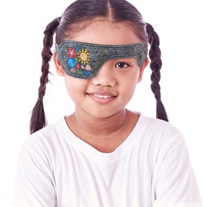 May include: A charcoal gray felt eye patch featuring colorful embroidered motifs including a yellow sun, a red flower, a blue swirl, and several small fish in various colors. The patch is shaped to cover one eye and has visible white stitching.