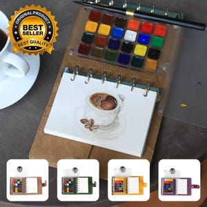Puede incluir: Un cuaderno de bocetos de acuarela encuadernado en cuero marrón con una ilustración de una taza de café. El cuaderno incluye una paleta de acuarela con varios colores y un pincel negro. La imagen también muestra una taza de café y el texto "ORIGINAL PRODUCT BEST SELLER BEST QUALITY".