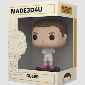 May include: A collectible figure of a soccer player in a white uniform with pink shoes, displayed in a box. The box has the text "MADE3D4U" and "GULER". The box is beige with a clear window showing the figure.
