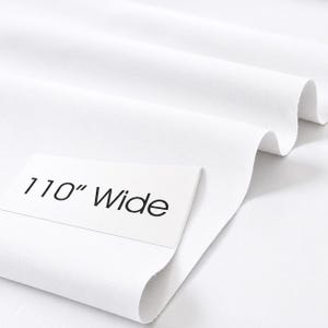 May include: A solid white fabric draped in soft folds, featuring a rectangular white label placed on the surface with the black printed text 110" Wide, indicating the width of the material in inches as shown on the label.