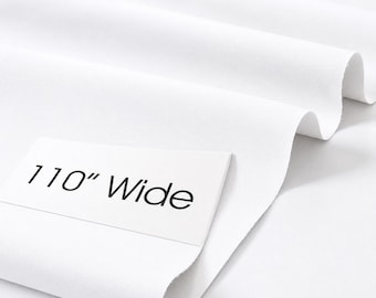 May include: A solid white fabric draped in soft folds, featuring a rectangular white label placed on the surface with the black printed text 110" Wide, indicating the width of the material in inches as shown on the label.