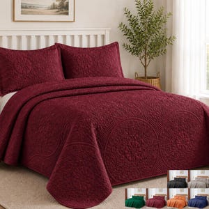 May include: A deep burgundy bedspread and two matching pillow shams featuring an intricate embossed circular medallion pattern. The bedding set is displayed on a bed, with smaller thumbnail images showing the same set in black, gray, green, and orange.
