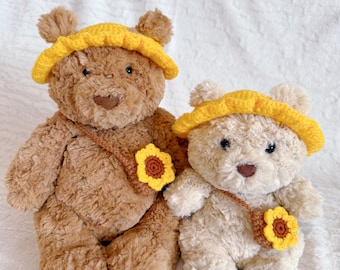 Pode incluir: Dois ursos de pelúcia, um castanho e outro creme, são exibidos. Cada urso usa um chapéu amarelo de crochê e uma bolsa transversal marrom adornada com um girassol amarelo e marrom. Os ursos estão em uma superfície branca texturizada.