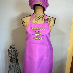 May include: A purple apron and matching chef hat set. The hat features the text Lil' Red. The apron displays the name Scarlett, the text EST. 2020, and a graphic of the character Eevee wearing a flower crown, with the Pok&eacute;mon logo below.