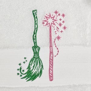 May include: A white towel with green and pink embroidered images of a broom and a wand with stars.