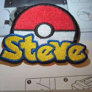 May include: An embroidered patch featuring a circular red and white ball design with a central black and white circle. Below the ball, the name Steve is stitched in yellow thread with a thick blue border, creating a bold, colorful graphic.