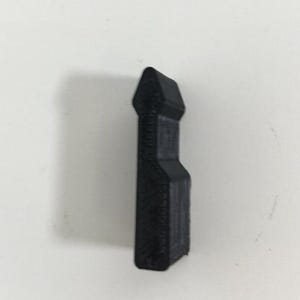 May include: A black, 3D-printed object with a rectangular body and a triangular top. The object has a textured surface and appears to be a small, decorative item. The background is plain white.