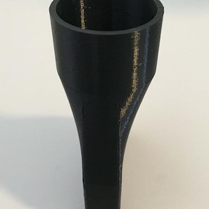 Puede incluir: Un embudo negro con una parte superior cilíndrica ancha y una base rectangular cónica. El interior es hueco y el exterior muestra líneas de capa de impresión 3D. El objeto está hecho de un material negro mate.