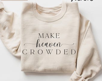 May include: A sand-coloured crewneck sweatshirt featuring the black printed text MAKE heaven CROWDED. The word heaven is written in a cursive script font, while MAKE and CROWDED are in a bold, capitalised serif font on the front chest.
