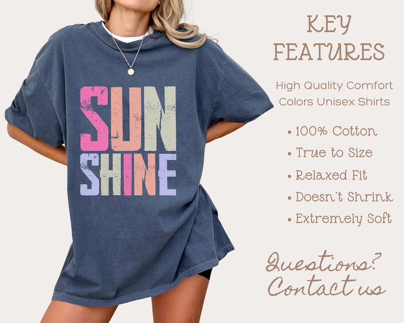 May include: A navy blue unisex t-shirt with the word "SUNSHINE" in colorful, distressed lettering. The shirt features a relaxed fit and is made of 100% cotton. Additional text on the right side lists key features of the shirt.