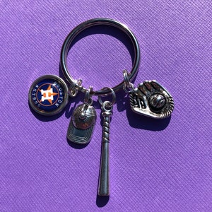 May include: A silver keychain with a baseball theme. It features a Houston Astros logo charm, a baseball bat charm, a baseball cap charm, and a baseball glove charm.