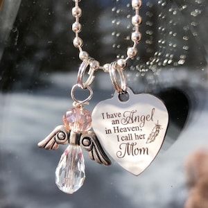 May include: Silver chain necklace with a heart-shaped pendant that reads "I have an Angel in Heaven, I call her Mom". A crystal angel charm hangs from the chain.
