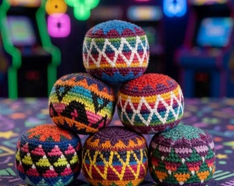 Könnte beinhalten: Ein Stapel von sechs bunten Hacky-Säcken. Jeder Ball hat ein einzigartiges Muster aus leuchtenden Farben, darunter Blau, Rot, Orange und Grün, mit geometrischen Designs. Der Hintergrund zeigt Spielautomaten und Neonlichter.