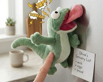 Könnte beinhalten: Ein grüner Plüschdinosaurier mit langer rosa Zunge, der an einem Kühlschrank befestigt ist. Der Dinosaurier hat große Augen und ist so positioniert, als würde er den Kühlschrank lecken. Textblasen sagen "ZAP!" und "SQUEAK!". Eine Einkaufsliste ist angebracht.