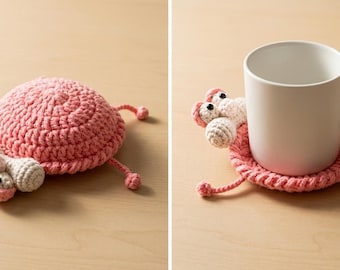 Könnte beinhalten: Ein rosa gehäkelter Untersetzer in Form eines skurrilen Wesens mit rundem Körper, vier Beinen und zwei großen Kulleraugen. Der Untersetzer ist für eine Tasse konzipiert, wie im Bild gezeigt.