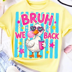 May include: A light yellow t-shirt featuring a graphic of a white duck wearing heart-shaped sunglasses that say TEACHER. The duck is blowing a pink bubble and holding a pink cup. The text BRUH WE BACK is printed in pink above and beside the duck.
